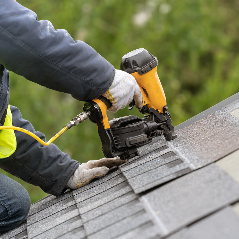 man nailing shingles on a roof